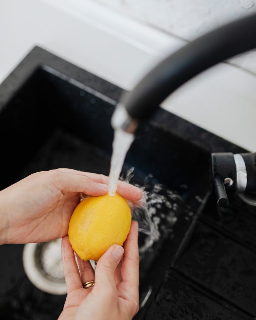 lemon being rinsed under a water faucet